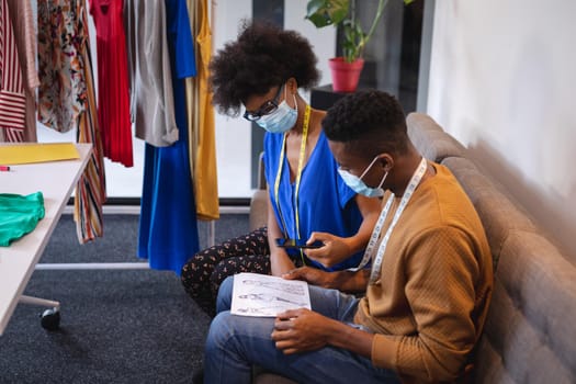 Diverse male and female fashion designers at work sitting on sofa discussing and looking at sketches. independent creative design business.