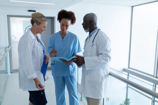 Three diverse male and female doctors standing in hospital corridor looking at medical documentation. medicine, health and healthcare services.