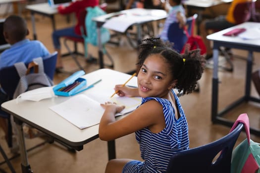 Portrait of african american girl smiling while sitting on her desk in class at elementary school. school and education concept