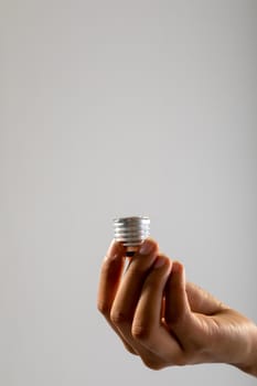 Close up of hand holding bulb screw base against grey background. business, professionalism and technology concept