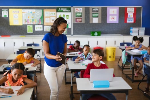 African american female teacher teaching caucasian boy to use digital tablet at elementary school. school and education concept