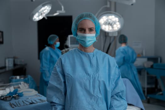 Portrait of caucasian female surgeon wearing face mask, surgical cap and gown in operating theatre. medicine, health and healthcare services during covid 19 coronavirus pandemic.