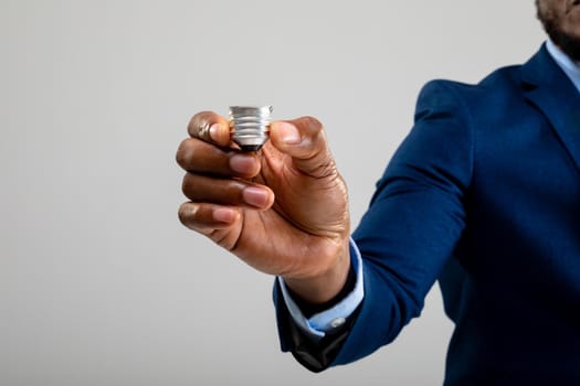 Mid section of businessman holding bulb screw base against grey background. business, professionalism and technology concept