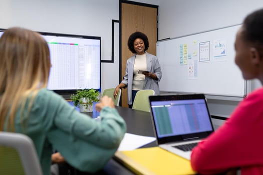 African american businesswoman giving presentation to diverse group of colleagues in meeting room. business in a modern office.