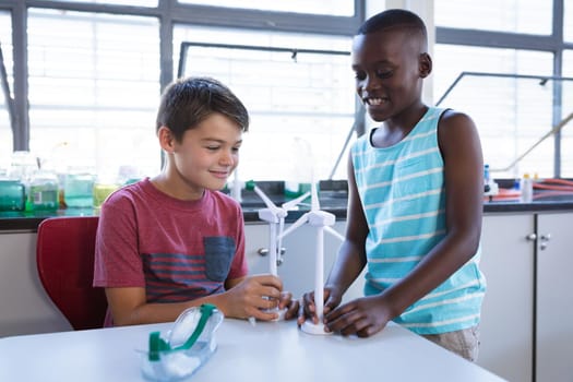 Caucasian boy and african american boy holding windmill models in science class at elementary school. school and education concept