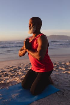 Senior african american man with folded hands meditating and practicing yoga at the beach. fitness yoga and healthy lifestyle concept