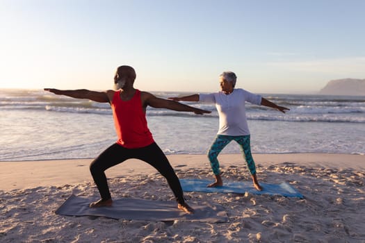 Senior african american couple performing stretching exercise together at the beach. fitness yoga and healthy lifestyle concept