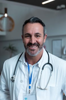 Portrait of smiling caucasian male doctor with stethoscope wearing lab coat in hospital. medicine, health and healthcare services during covid 19 coronavirus pandemic.