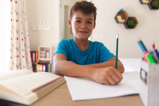Smiling caucasian boy having video call during class, sitting at desk at home. online schooling, distance learning and education at home.