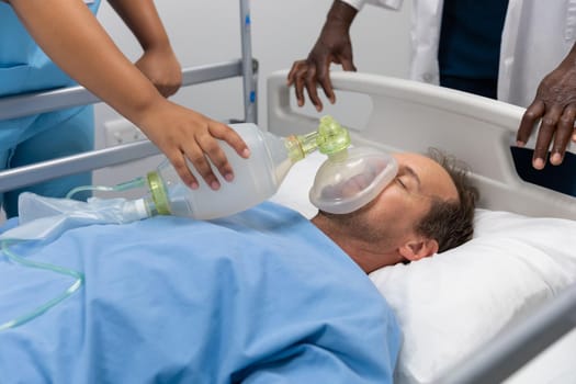 Diverse male and female doctors putting oxygen mask on patient lying in bed. medicine, health and healthcare services during coronavirus covid 19 pandemic.