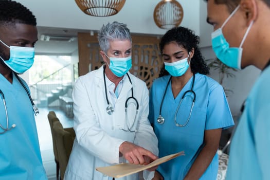 Caucasian female senior doctor and diverse hospital colleagues wearing face masks talking at meeting. medicine, health and healthcare services during covid 19 coronavirus pandemic.