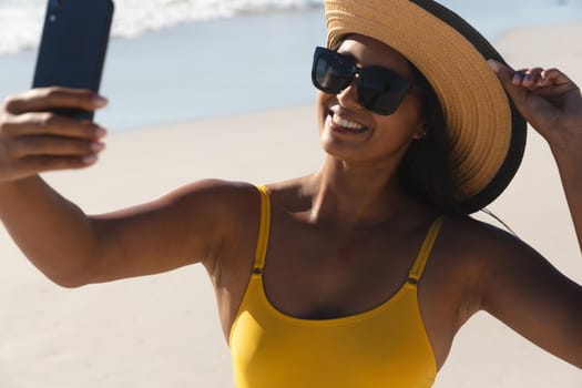 Smiling mixed race woman on beach holiday taking selfie. outdoor leisure vacation time by the sea.