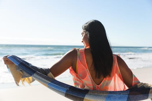 Smiling mixed race woman on beach holiday wearing shawl. outdoor leisure vacation time by the sea.