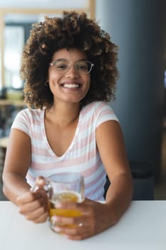 Portrait of mixed race woman sitting at table smiling having beer. friends socialising and drinking at bar.