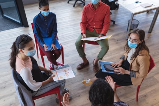 Diverse group of creative colleagues wearing face masks talking at meeting. work at a modern office during covid 19 coronavirus pandemic.