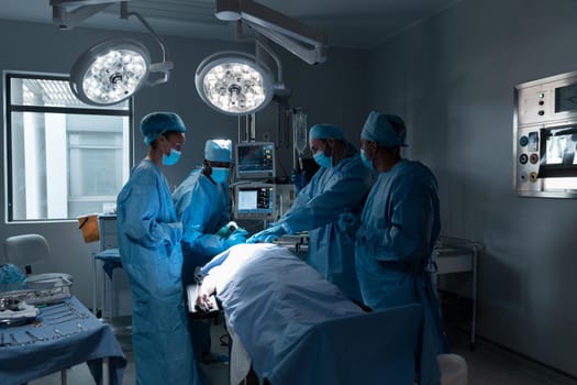 Diverse male and female doctors wearing face masks and surgical overalls in operating theatre. medicine, health and healthcare services during coronavirus covid 19 pandemic.