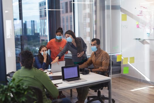 Diverse group of creative colleagues wearing face masks talking at meeting. work at a modern office during covid 19 coronavirus pandemic.