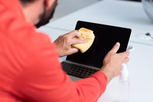 Midsection of businessman disinfecting laptop with special spray. independent creative business during covid 19 coronavirus pandemic.