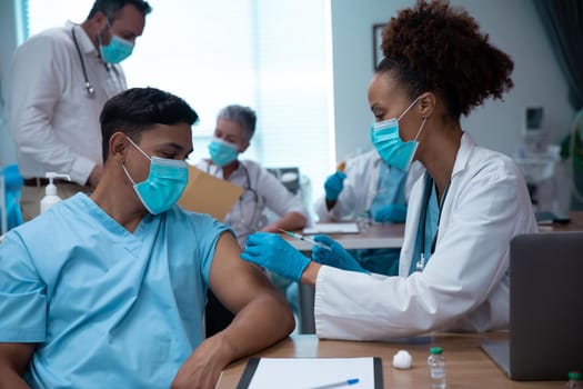 Mixed race couple of doctors wearing face masks making injection. medicine, health and healthcare services during coronavirus covid 19 pandemic.