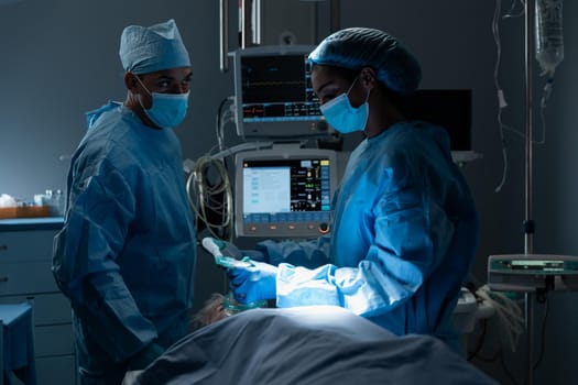 Diverse surgeons with face masks and protective clothing during operation, sedating patient. operating theatre. medicine, health and healthcare services during covid 19 coronavirus pandemic.