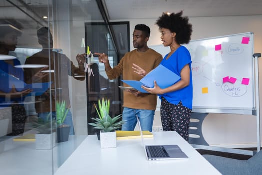 Diverse male and female colleagues standing having discussion with whiteboard in background. independent creative design business.