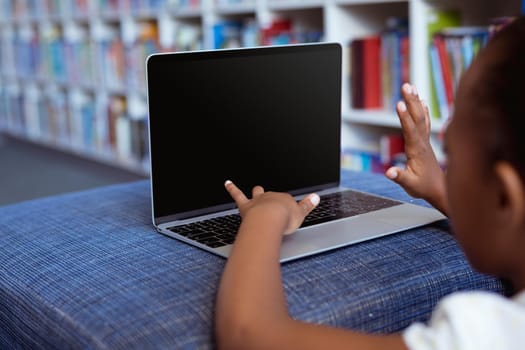 African american schoolgirl at desk in school library using laptop, with copy space on screen. childhood, technology and education at elementary school.