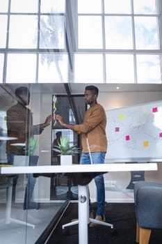 African american businessman sticking memo notes on glass wall with whiteboard in background. independent creative design business.