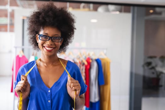 Portrait of happy mixed race fashion designer working in office with tailor centimeter on neck. independent creative design business.