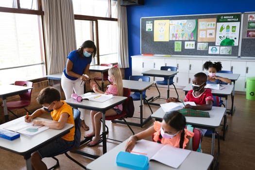 African american female teacher spraying hand sanitizer on hands of girl at elementary school. education back to school health safety during covid19 coronavirus pandemic