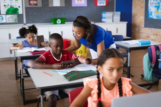 African american female teacher teaching a boy to use digital tablet in class at elementary school. school and education concept