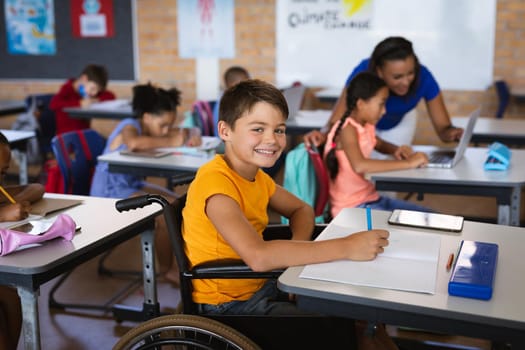 Portrait of disabled caucasian boy smiling while sitting on wheelchair in class at elementary school. school and education concept