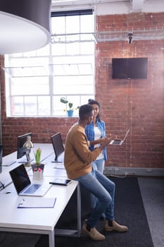 Diverse male and female colleagues at work standing discussing over laptop. independent creative design business.