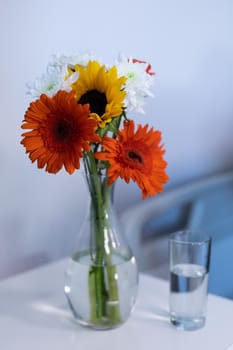 Colourful gerbera flowers in a vase, and a glass of water on a hospital patient's bedside table. medicine, health and healthcare services.