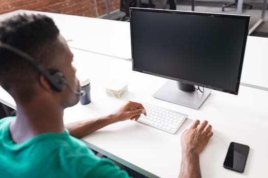 African american businessman having video call sitting in front of computer using headphones. independent creative design business.