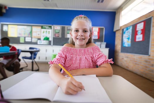 Portrait of caucasian girl smiling while sitting on her desk in the class at school. school and education concept