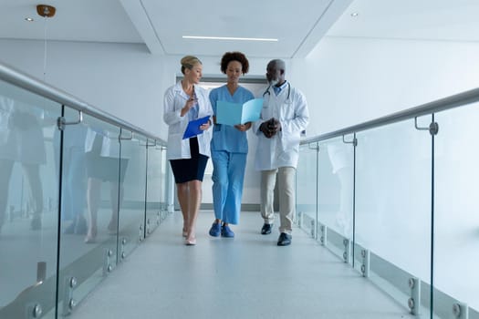 Three diverse male and female doctors walking through hospital corridor looking at document. medicine, health and healthcare services.