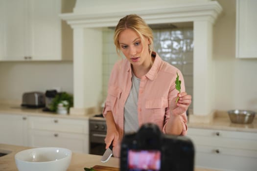 Caucasian woman in kitchen preparing food, holding salad leaf to camera, making cooking vlog. technology and communication, cookery vlogger at home.