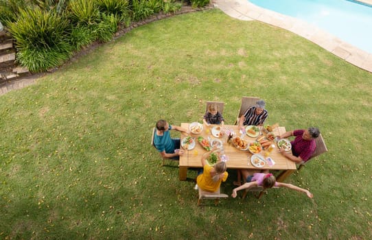 High angle view of caucasian three generation family sitting at table eating meal in garden. three generation family celebrating independence day eating outdoors together.