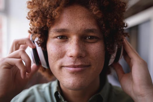 Portrait of happy mixed race businessman standing in office and wearing headphones. independent creative design business.