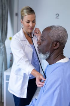 Caucasian female doctor examining with stethoscope african american male patient in hospital room. medicine, health and healthcare services
