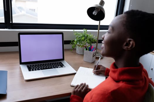 Happy african american businesswoman having video call writing notes using laptop with copy space. business in a modern office.