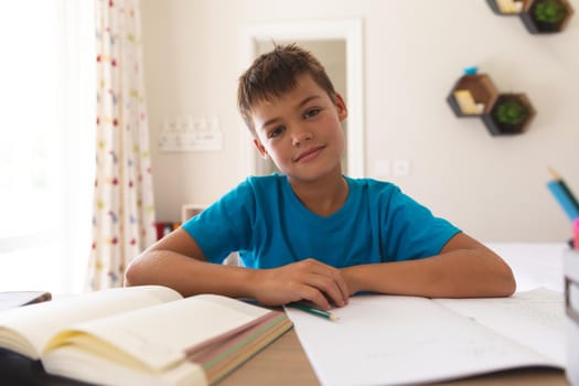 Smiling caucasian boy having video call during class, sitting at desk at home. online schooling, distance learning and education at home.