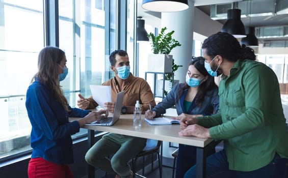 Diverse group of creative colleagues wearing face masks talking at meeting. work at a modern office during covid 19 coronavirus pandemic.