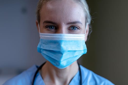 Portrait of caucasian female doctor wearing face mask and scrubs looking to camera. medical professional at work and health services during coronavirus covid 19 pandemic.