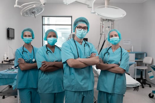 Diverse group of male and female doctors standing in operating theatre wearing face masks. medicine, health and healthcare services during coronavirus covid 19 pandemic.