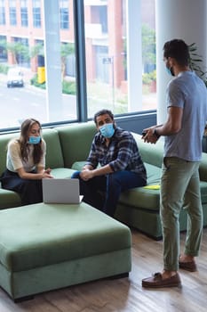 Diverse group of creative colleagues wearing face masks talking at meeting. work at a modern office during covid 19 coronavirus pandemic.