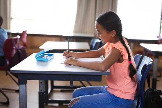 African american girl studying while sitting on her desk in the class at elementary school. school and education concept