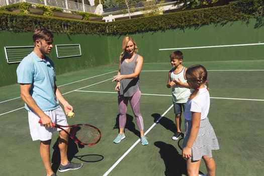 Happy caucasian couple with daughter and son outdoors, playing tennis on tennis court. family enjoying healthy free time activities together.