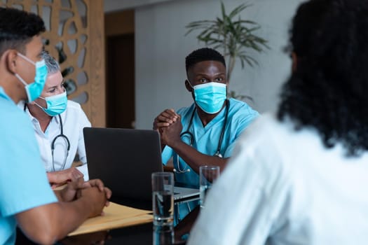 Diverse male and female doctors wearing face masks sitting in hospital having discussion. medicine, health and healthcare services during coronavirus covid 19 pandemic.