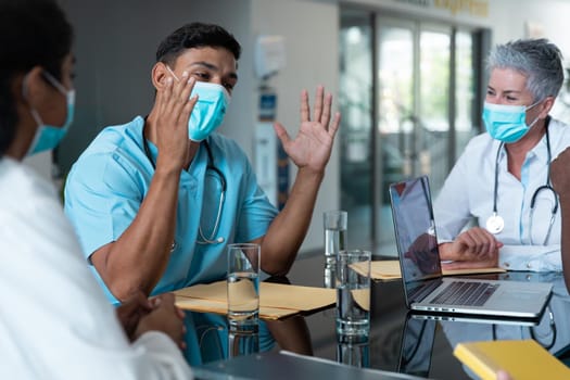 Diverse male and female doctors wearing face masks sitting in hospital having discussion. medicine, health and healthcare services during coronavirus covid 19 pandemic.